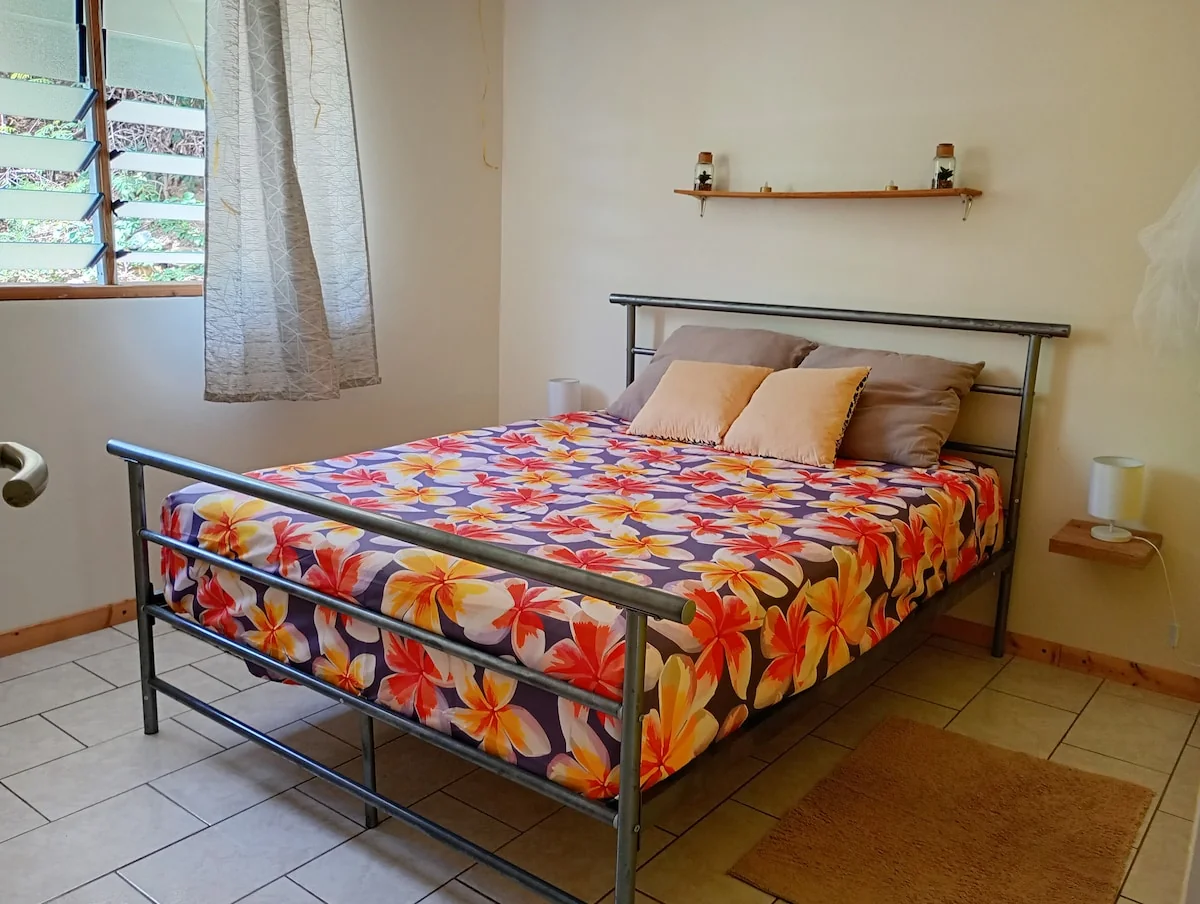 Bedroom with a double bed with a floral sheet and a louvred window