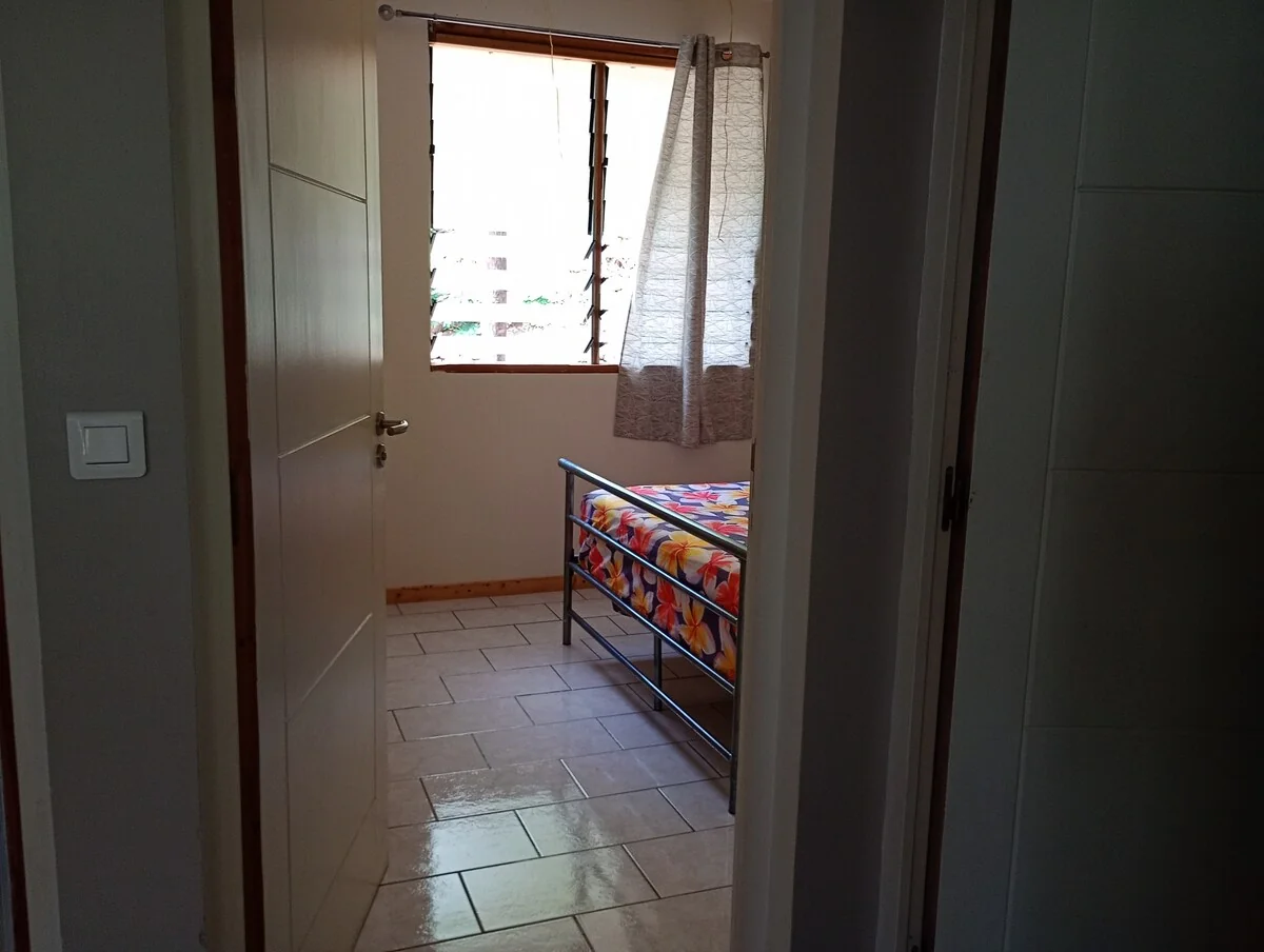 Open door onto the first bedroom: a double bed with a floral sheet under a curtained window