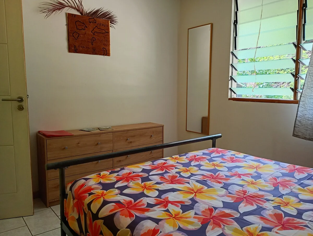 The first bedroom with a wooden chest of drawers, a large mirror and a louvred window onto the garden