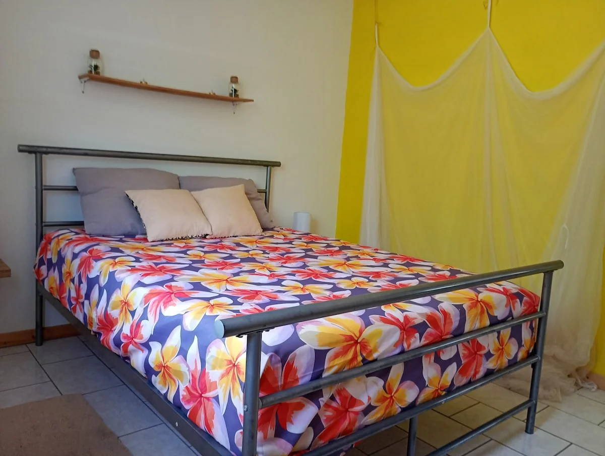 Bedroom with yellow walls, a double bed with a floral sheet and a mosquito net