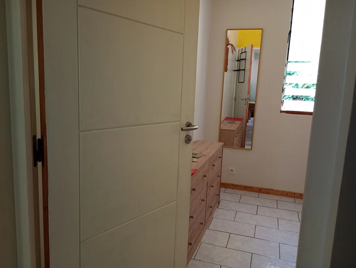 Bedroom entrance with a wooden chest of drawers and a large mirror by the window