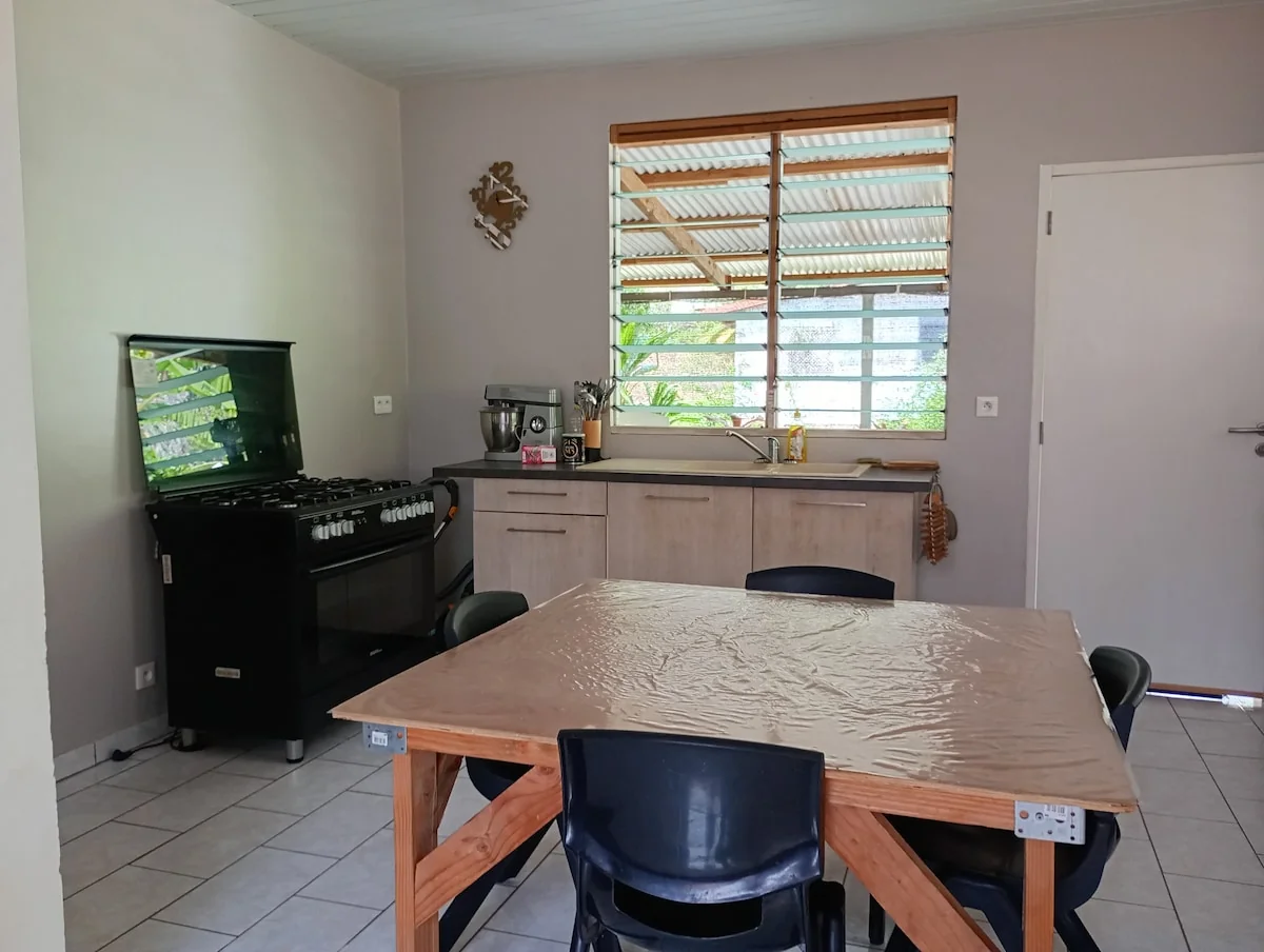 Fitted kitchen with a gas cooker, a worktop and a wooden table under a louvred window