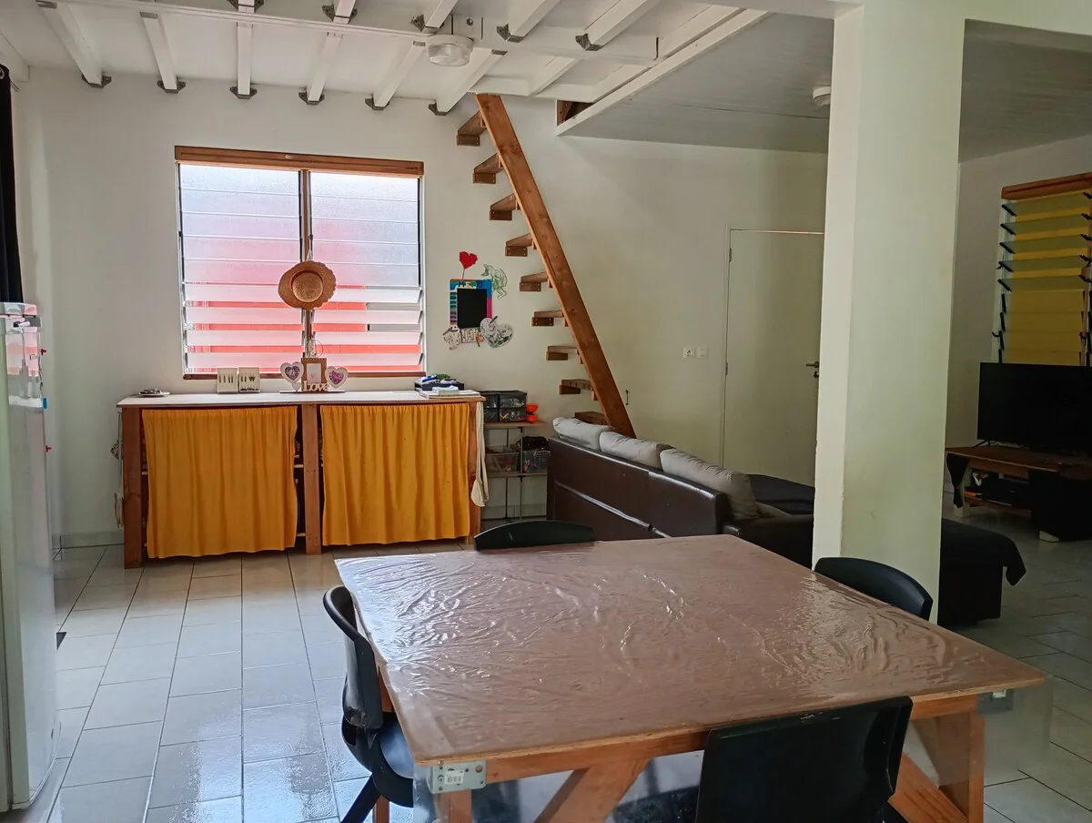 Living area with a large wooden table, a sofa, a wooden staircase and louvred windows