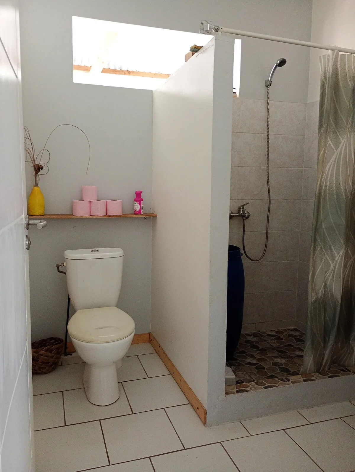 Toilet and pebble-floored shower, separated by a low wall, with a shower curtain
